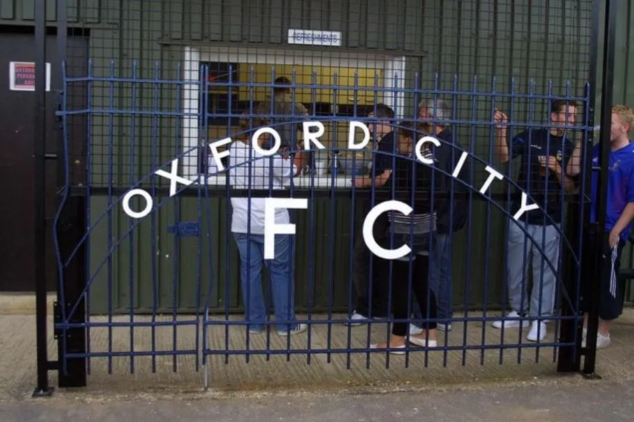 Hàng rào sân vận động Oxford City FC với biển hiệu kỷ niệm cổng Whitehouse Ground, minh chứng lịch sử của đội bóng