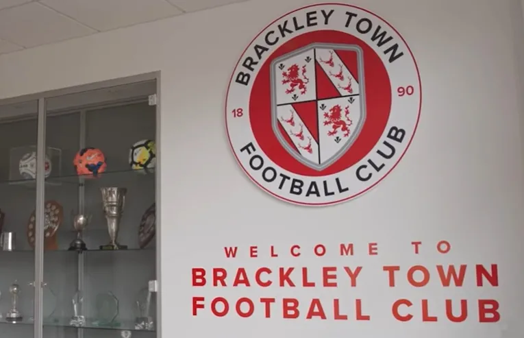 Logo và huy hiệu của câu lạc bộ bóng đá Brackley Town FC với hình ảnh thánh đường và màu đỏ trắng đặc trưng